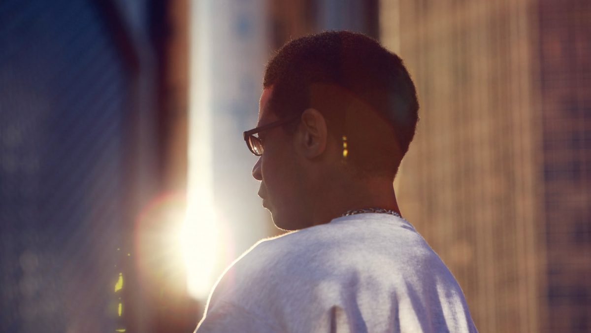 Person in profile wearing glasses, backlit in an alley